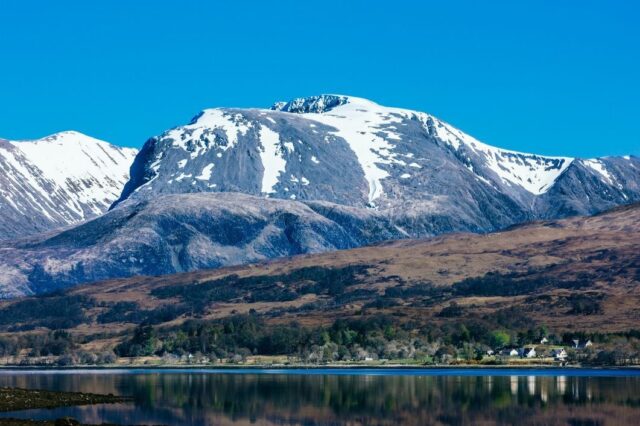 A photograph of the snow-capped Ben Nevis mountain under a clear blue sky, promoting a fully guided climb event.