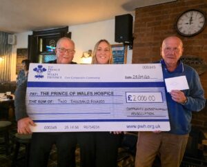 Three adults pose with an oversized £2,000 check made payable to The Prince of Wales Hospice.