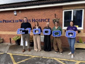 Five people outside the Prince of Wales Hospice hold large blue-and-white characters spelling “£1000.”
