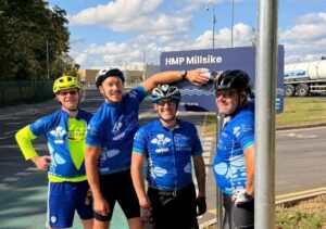 Tour de hmp cyclists posing with location sign