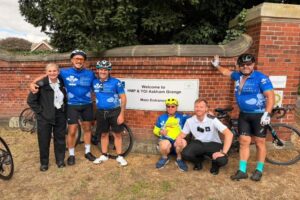 Tour de hmp cyclists posing with location sign