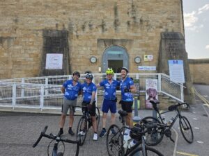 Tour de hmp cyclists posing with location sign