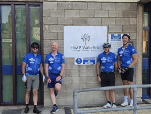 Tour de hmp cyclists posing with location sign