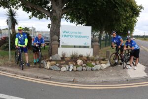Tour de hmp cyclists posing with location sign