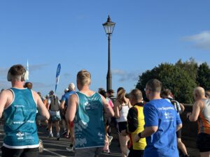 A group of runners and walkers wearing hospice-support shirts moves along a road beneath a tall streetlamp.